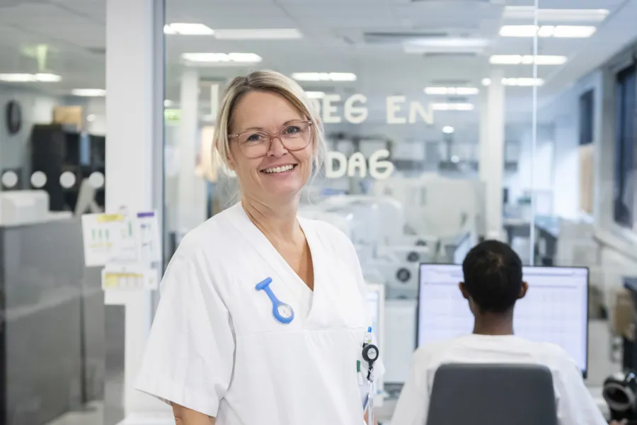 En hvitkledd kvinnelig sykehusansatt smiler mot kamera