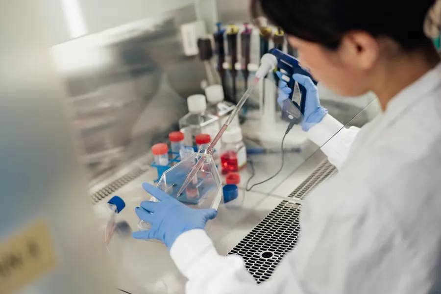 En person iført en hvit laboratoriefrakk og hansker som holder en sprøyte