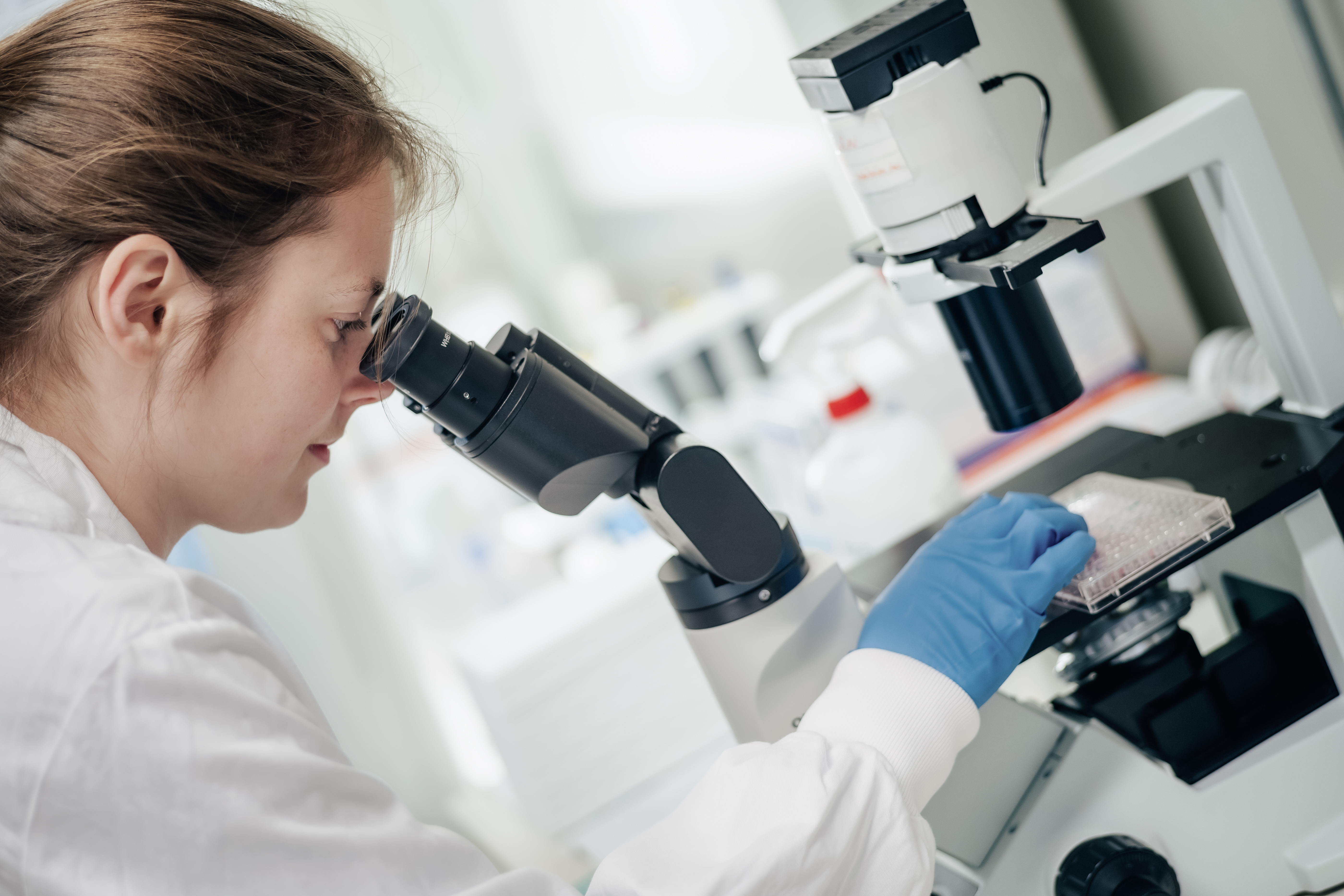En person i laboratoriefrakk som ser gjennom et mikroskop