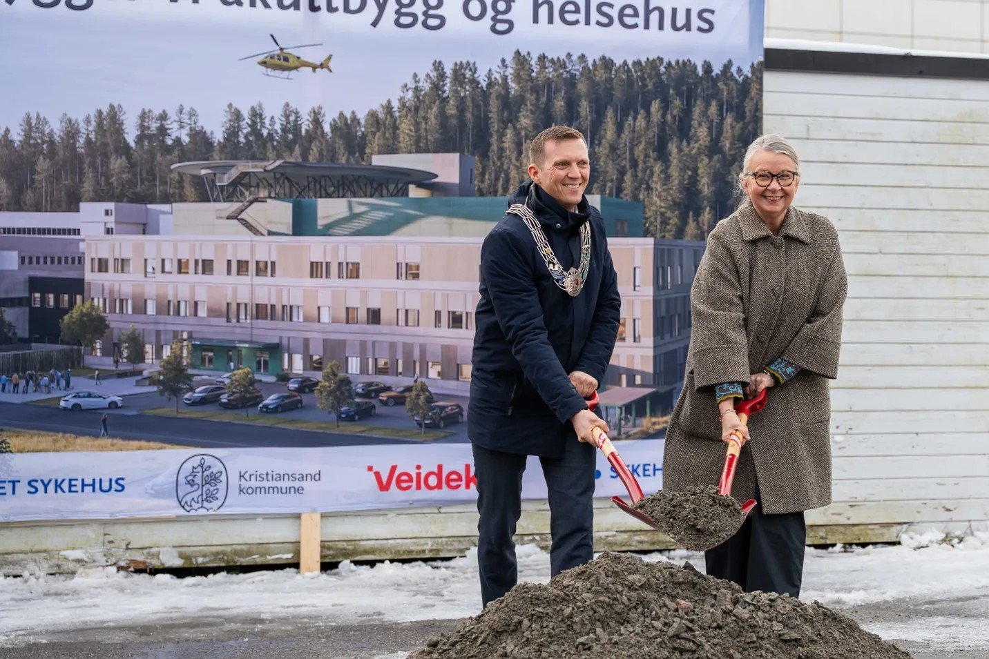 Ordfører og administrerende dør foran plansje av nytt sykehus med hver sin spade