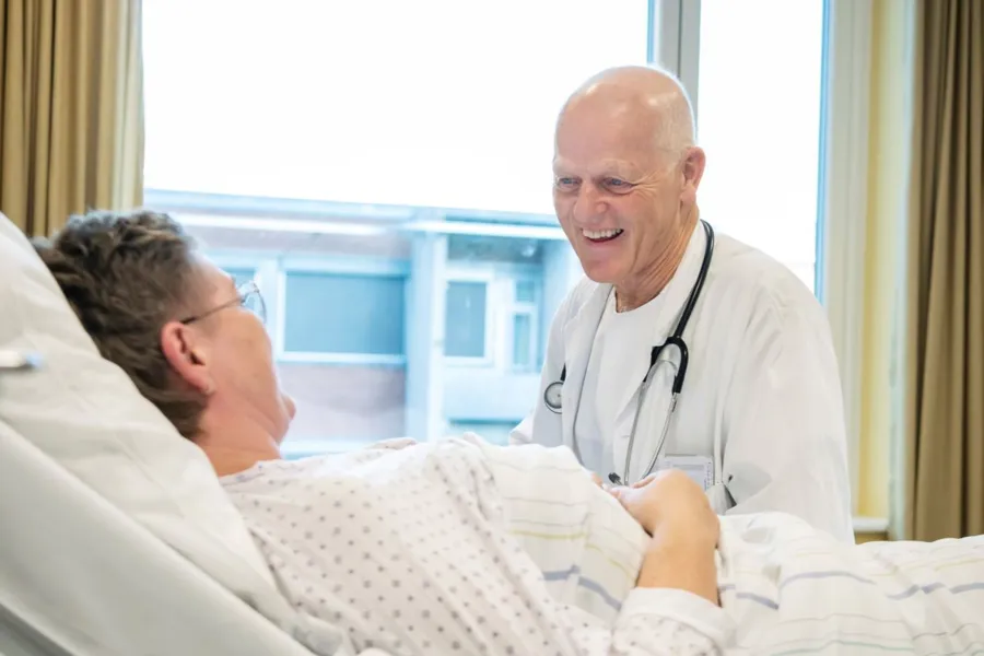 En mannlig mannlig lege som snakker med kvinnelig pasient som ligger i en sykehusseng.