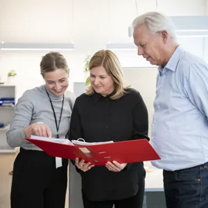 Tre kontoransatte ser sammen i en rød perm