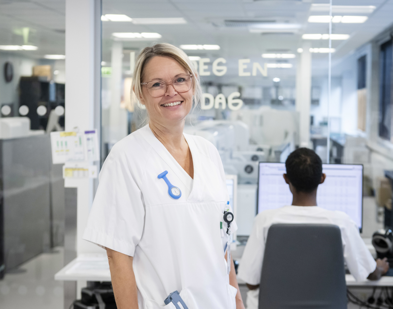 En hvitkledd kvinnelig sykehusansatt smiler mot kamera