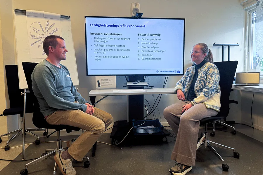 En mann og en kvinne sitter i stoler foran en projektorskjerm