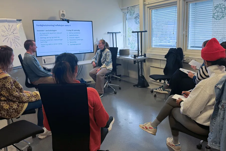 En gruppe mennesker som sitter i et rom og ser på en skjerm