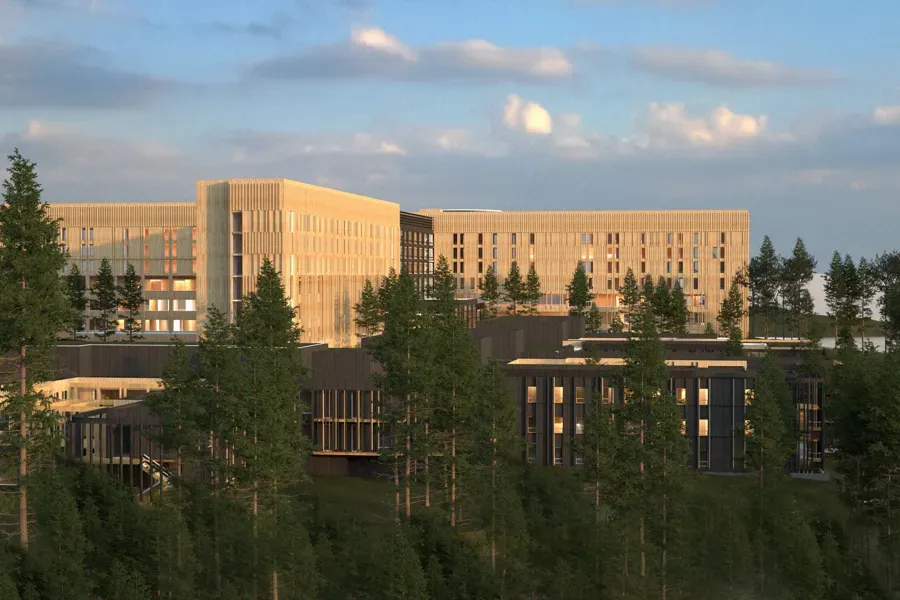 Et stort bygg i tre, med trær rundt og Mjøsa i det fjerne