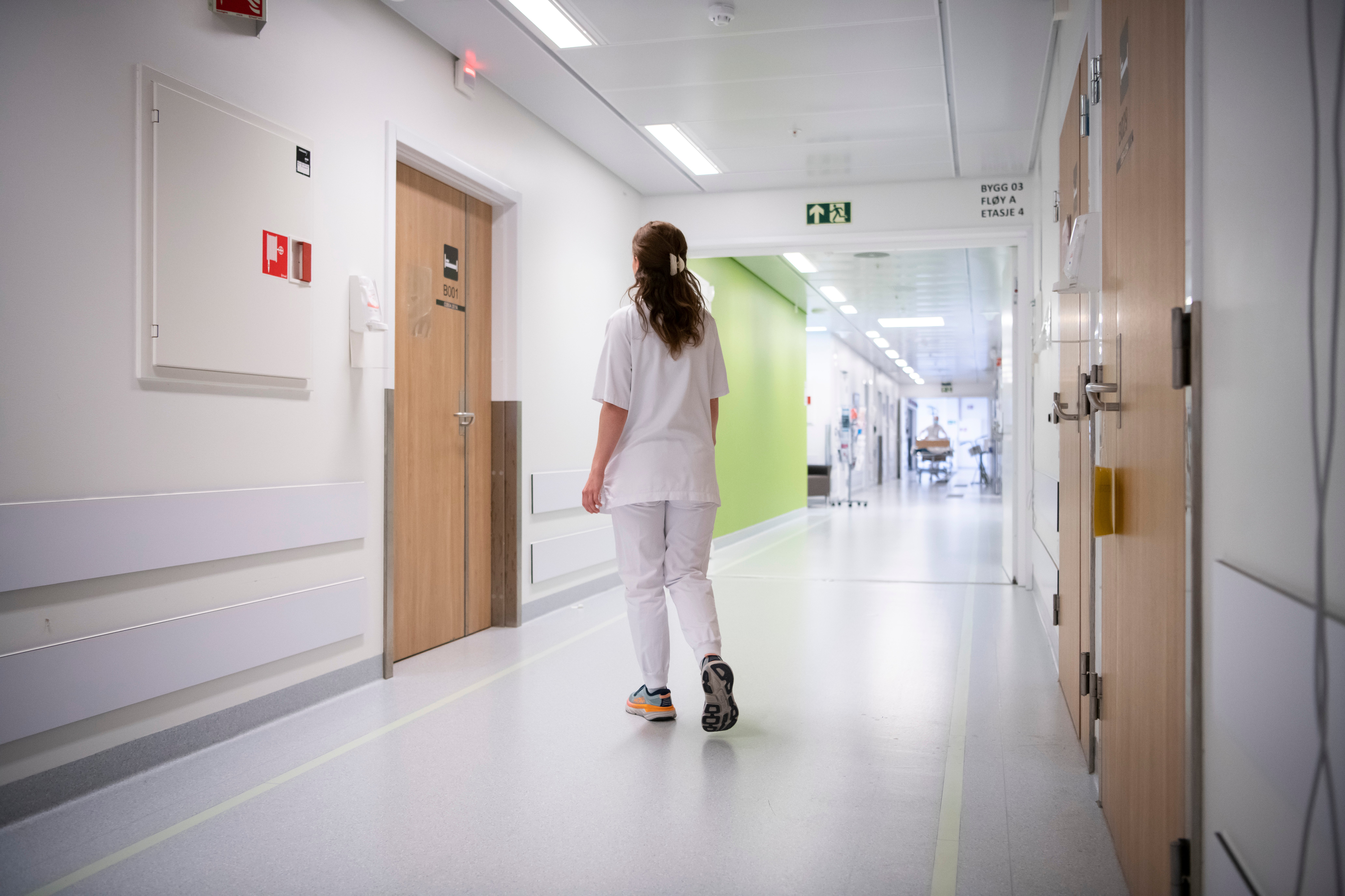 Sykepleier går i korridor med ryggen til