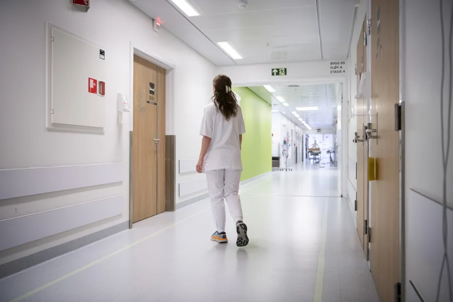 Sykepleier går i korridor med ryggen til