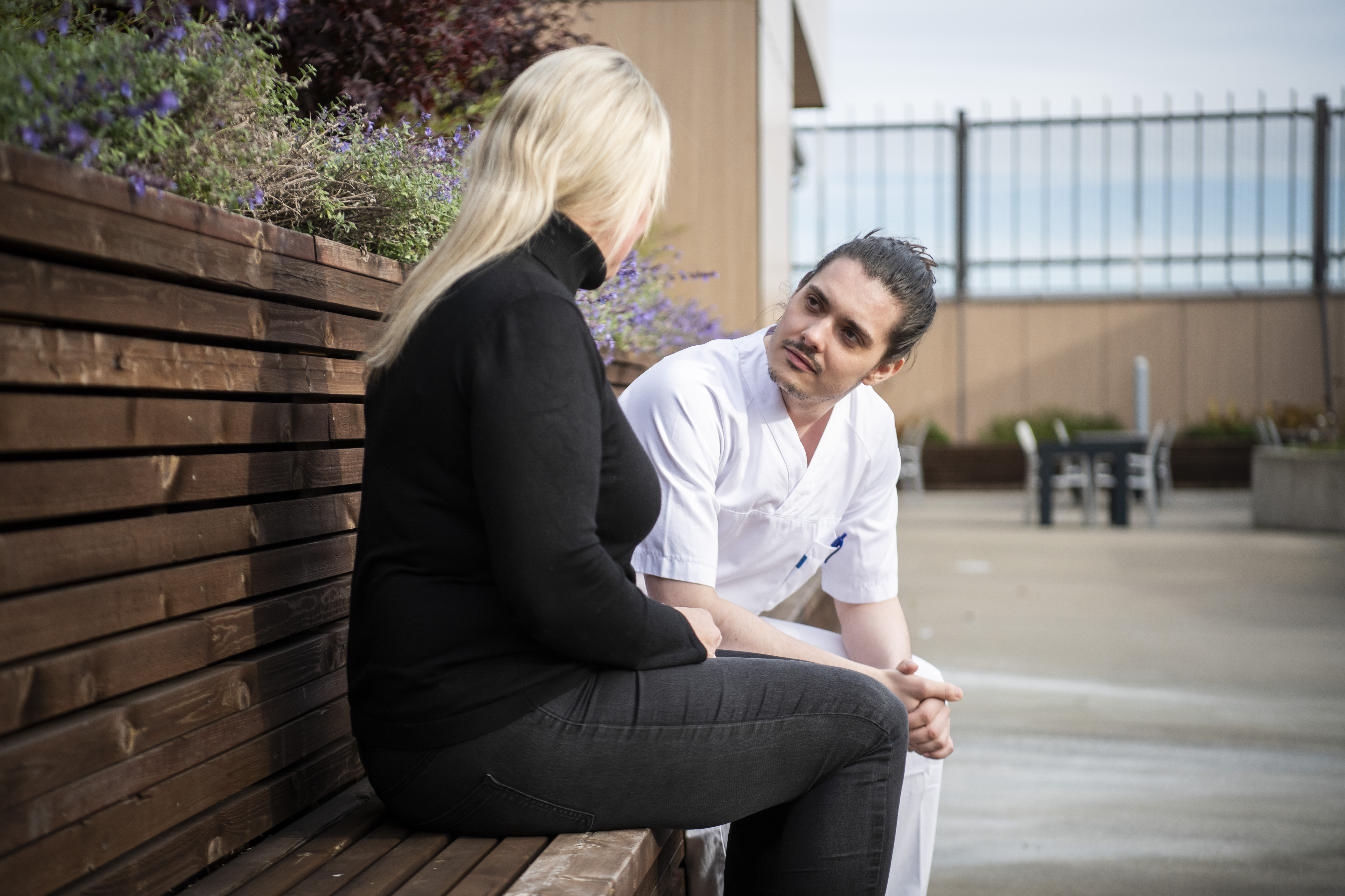 Ansatt og pasient sitter på benk ute og snakker