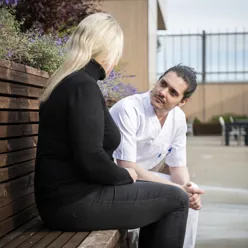 Ansatt og pasient sitter på benk ute og snakker