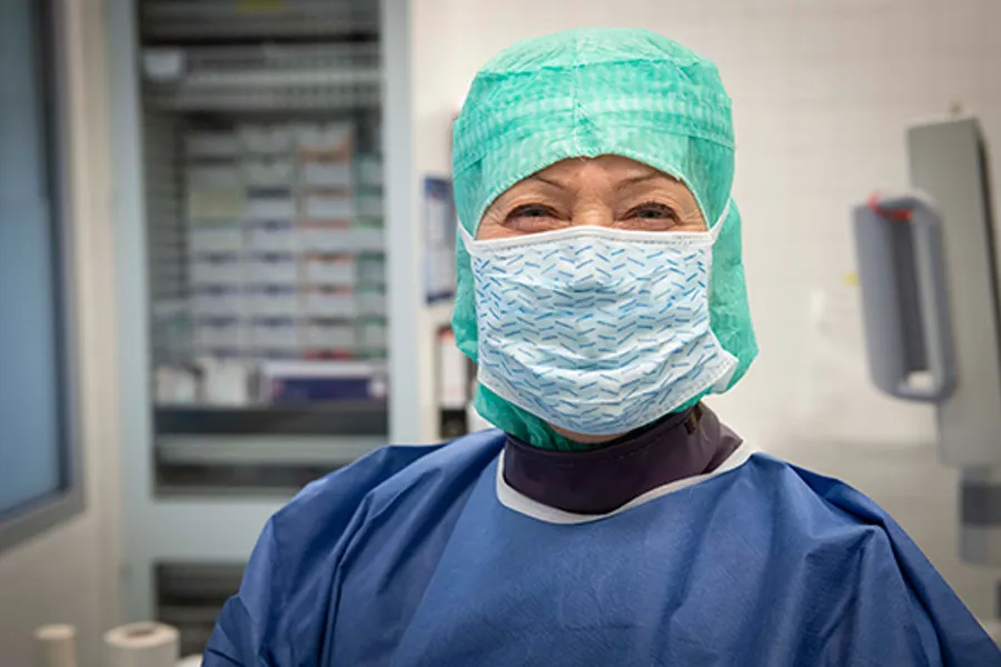 Blid ansatt i operasjonssal med lue og munnbind