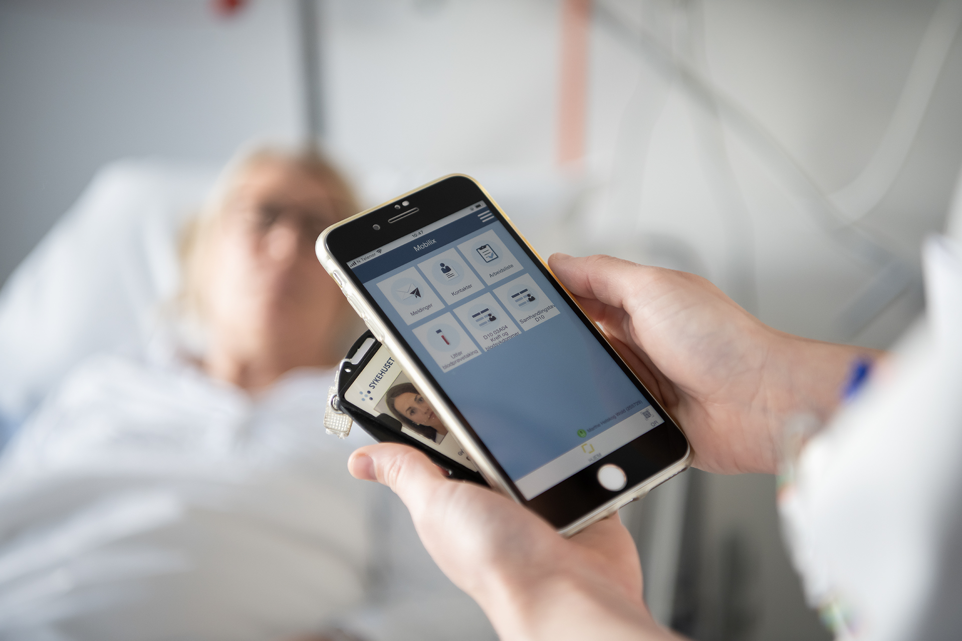 Hender som holder mobil og id kort, pasient i bakgrunnen