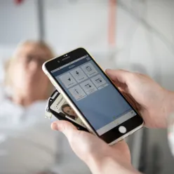 Hender som holder mobil og id kort, pasient i bakgrunnen