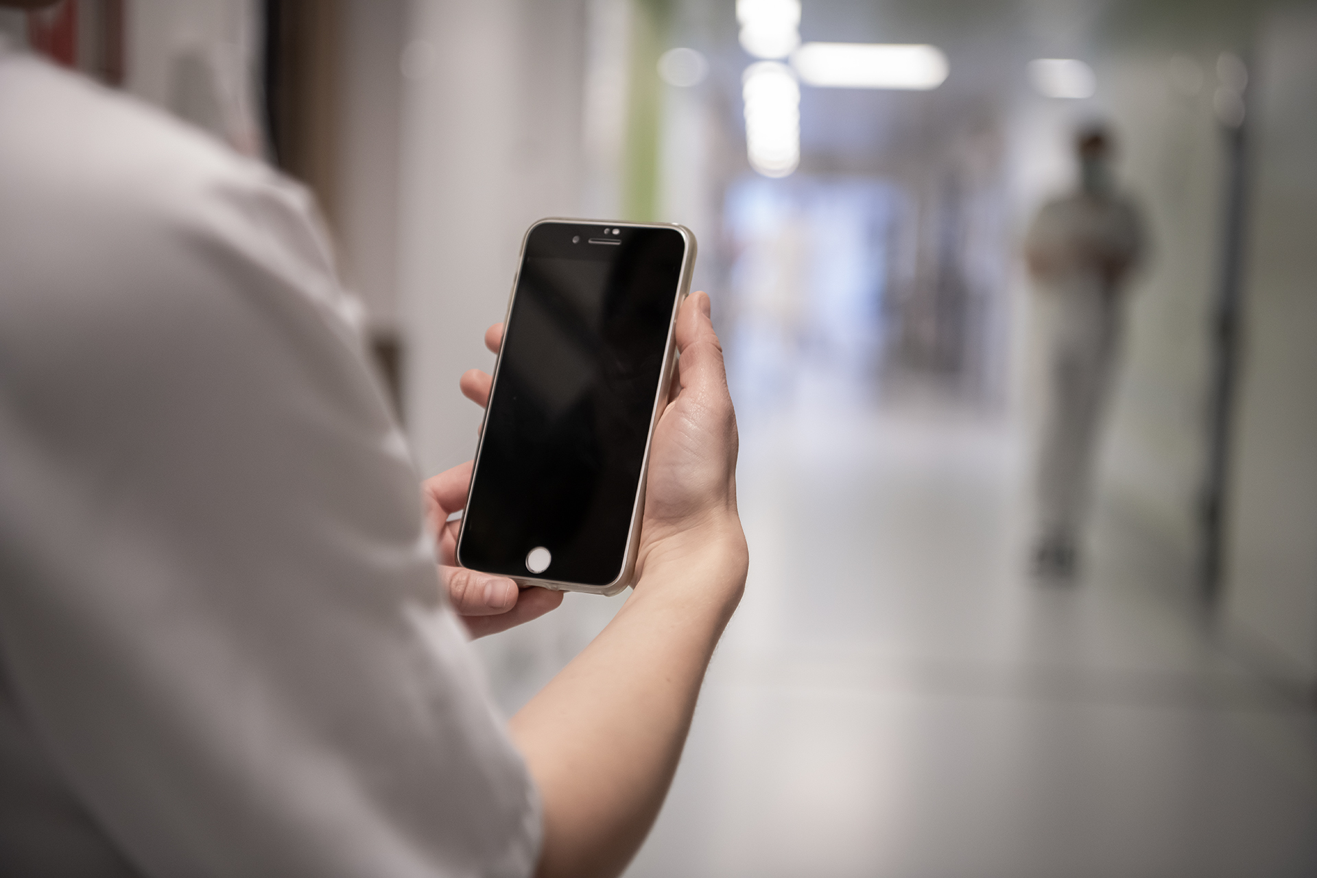 Hender som holder en tlf, korridor i bakgrunnen