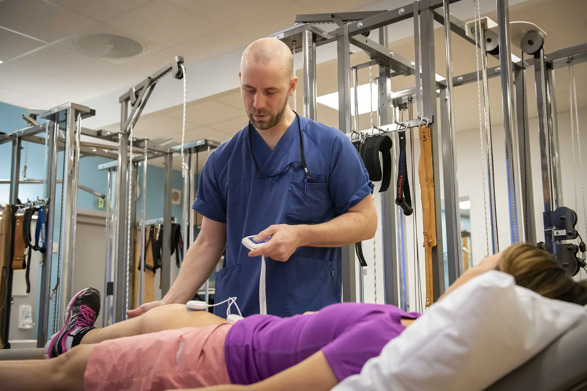 Pasient i treningstøy blir undersøkt på benk av fysioterapeut