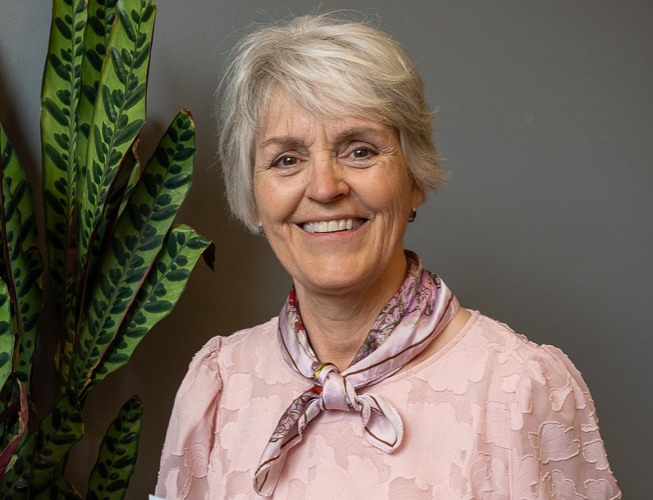 En person som smiler med en plante i bakgrunnen