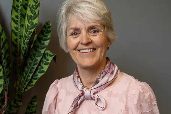 En person som smiler med en plante i bakgrunnen