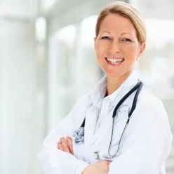 Smilende kvinnelig lege i frakk med stetoskop rundt halsen
