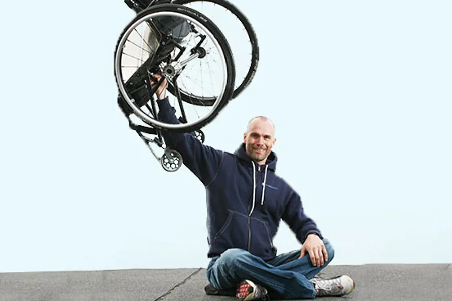 En mann som sitter på bakken med en sykkel i luften