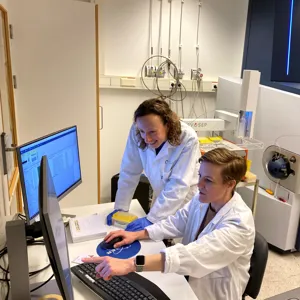 Et par personer i laboratoriefrakker som jobber med datamaskiner