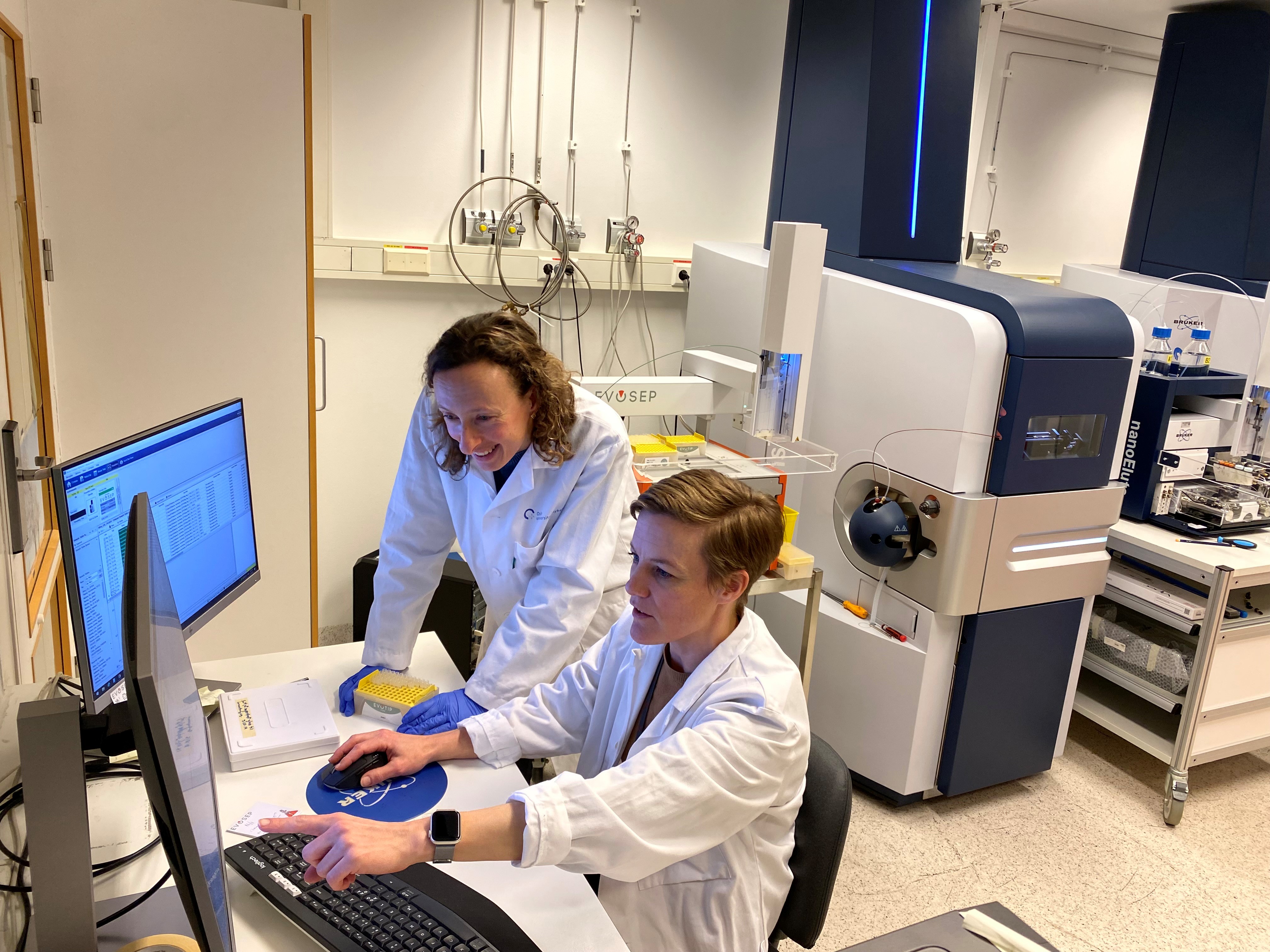 Et par personer i laboratoriefrakker som jobber med datamaskiner