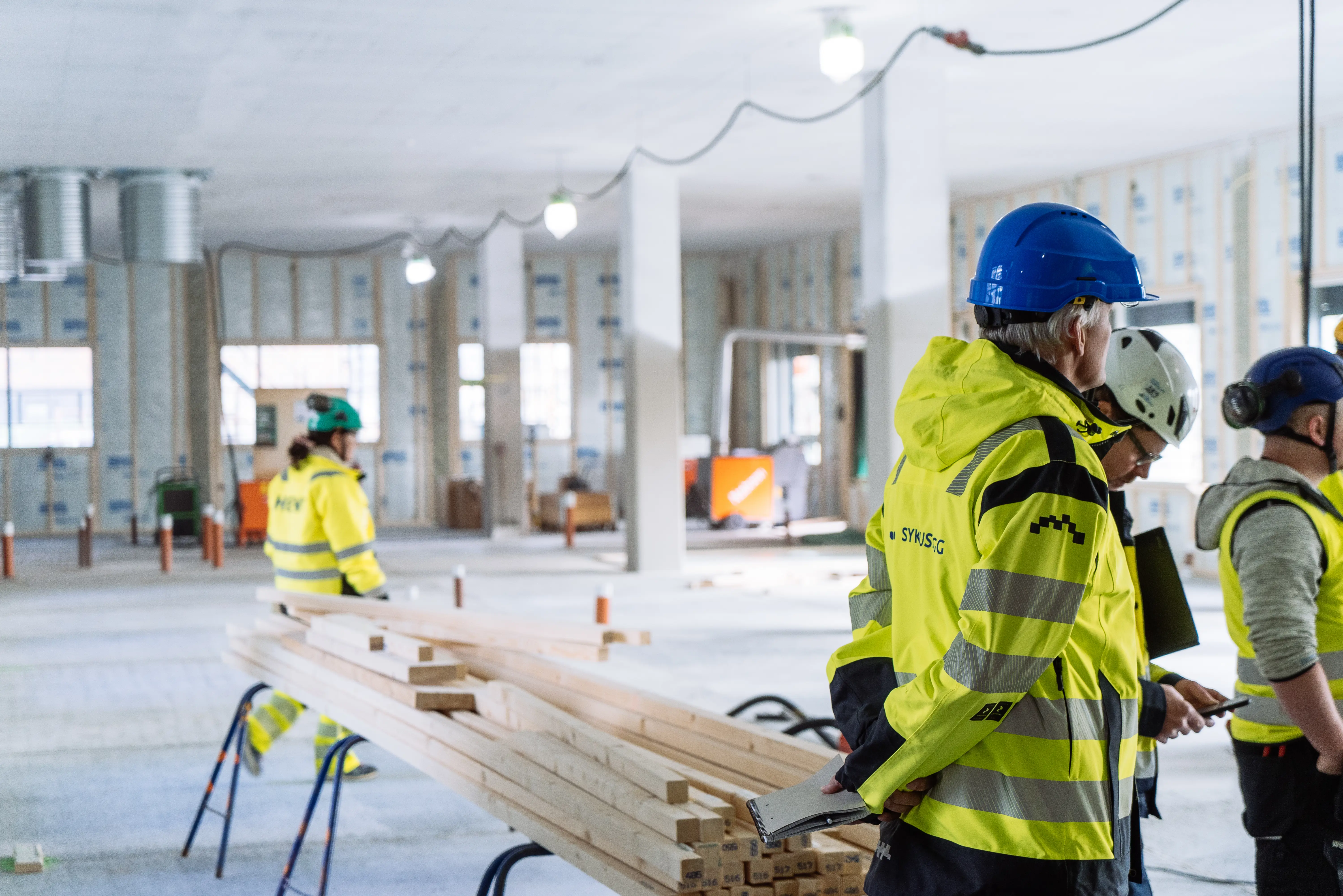Bilde av mennesker med gul jakke og hjelm inne i et uferdig bygg