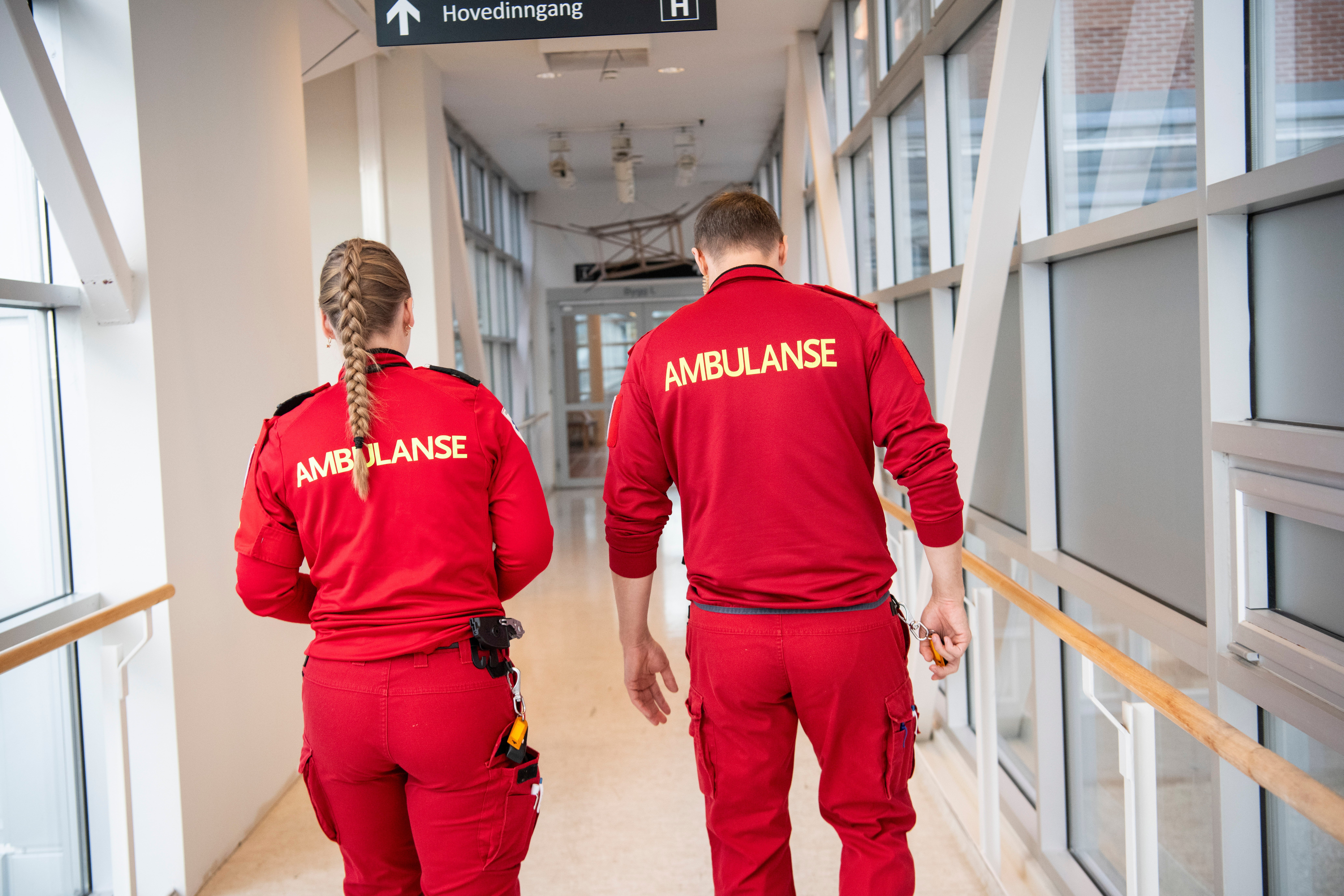 Mann og kvinne i rød ambulanseunifrom sett bakfra
