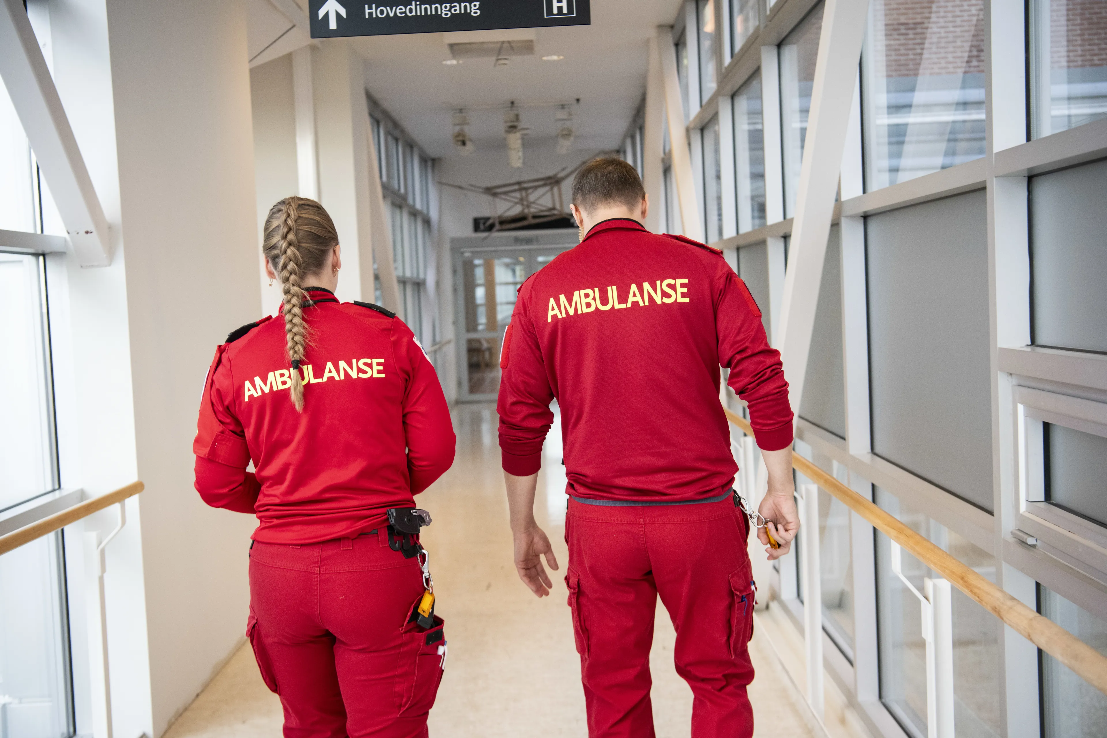Mann og kvinne i rød ambulanseunifrom sett bakfra