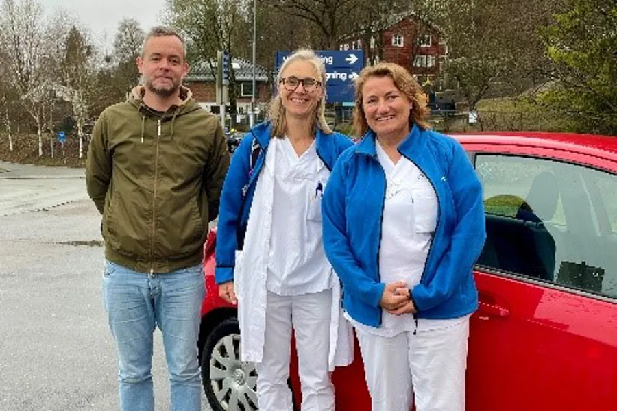 En gruppe mennesker som står ved siden av en rød bil