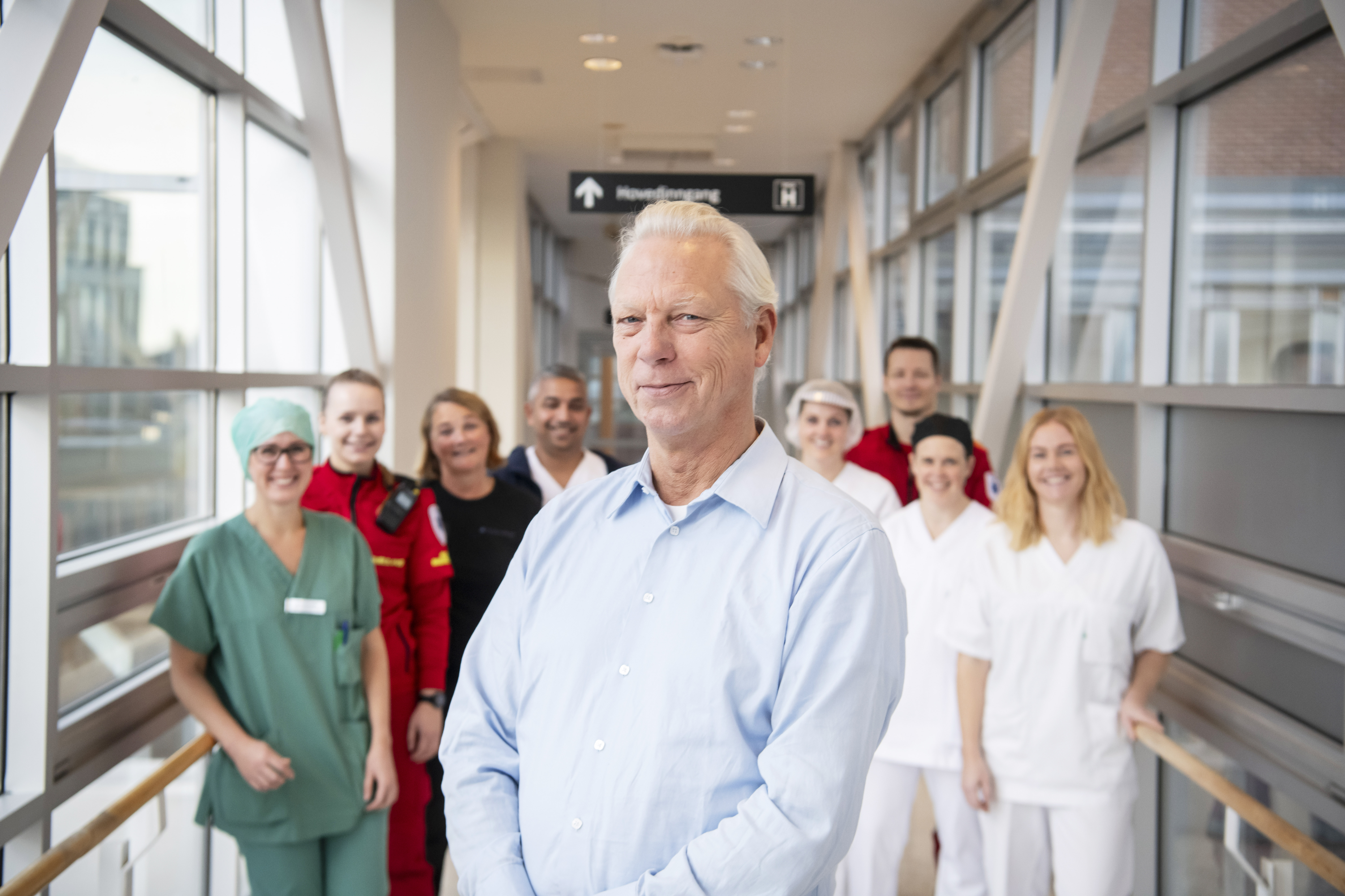 Mann i skjorte foran flere ansatte i forskjellige sykehusuniformer