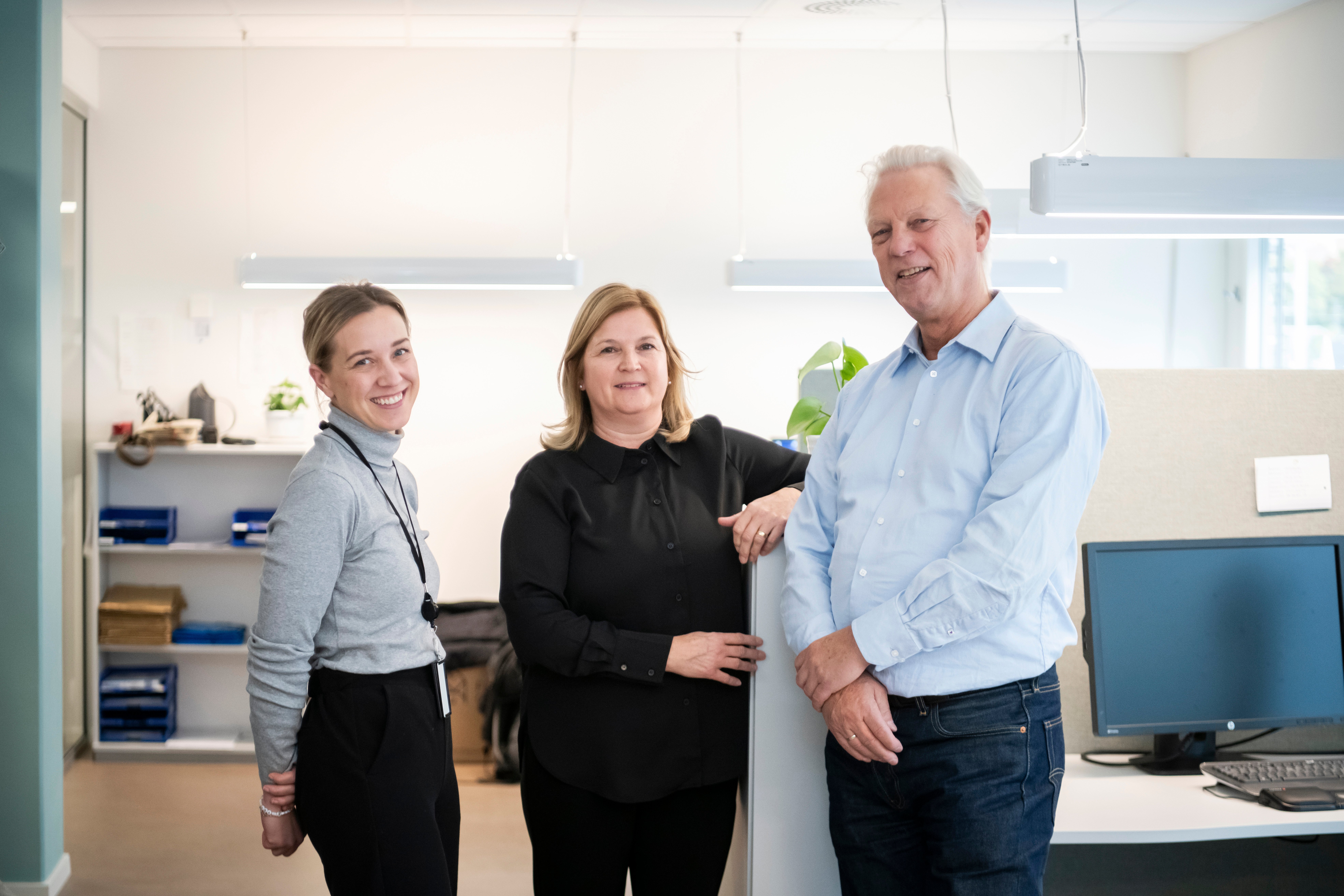 Tre kontoransatte smiler mot kamera