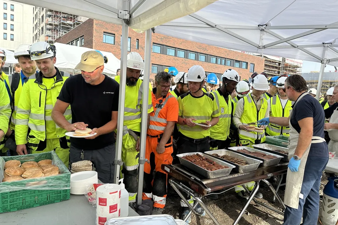 En gruppe mennesker iført sikkerhetsvester og hatter som står rundt en grill