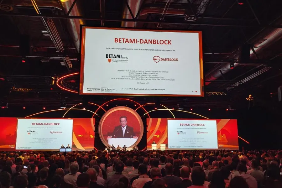 En gruppe mennesker som sitter i et rom med en scene og en stor skjerm