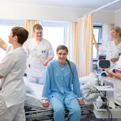 Pasient sitter på seng omgitt av 4 sykepleiere