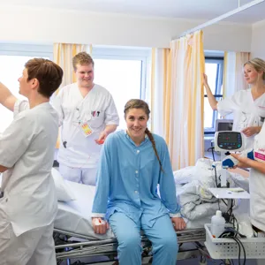 Pasient sitter på seng omgitt av 4 sykepleiere