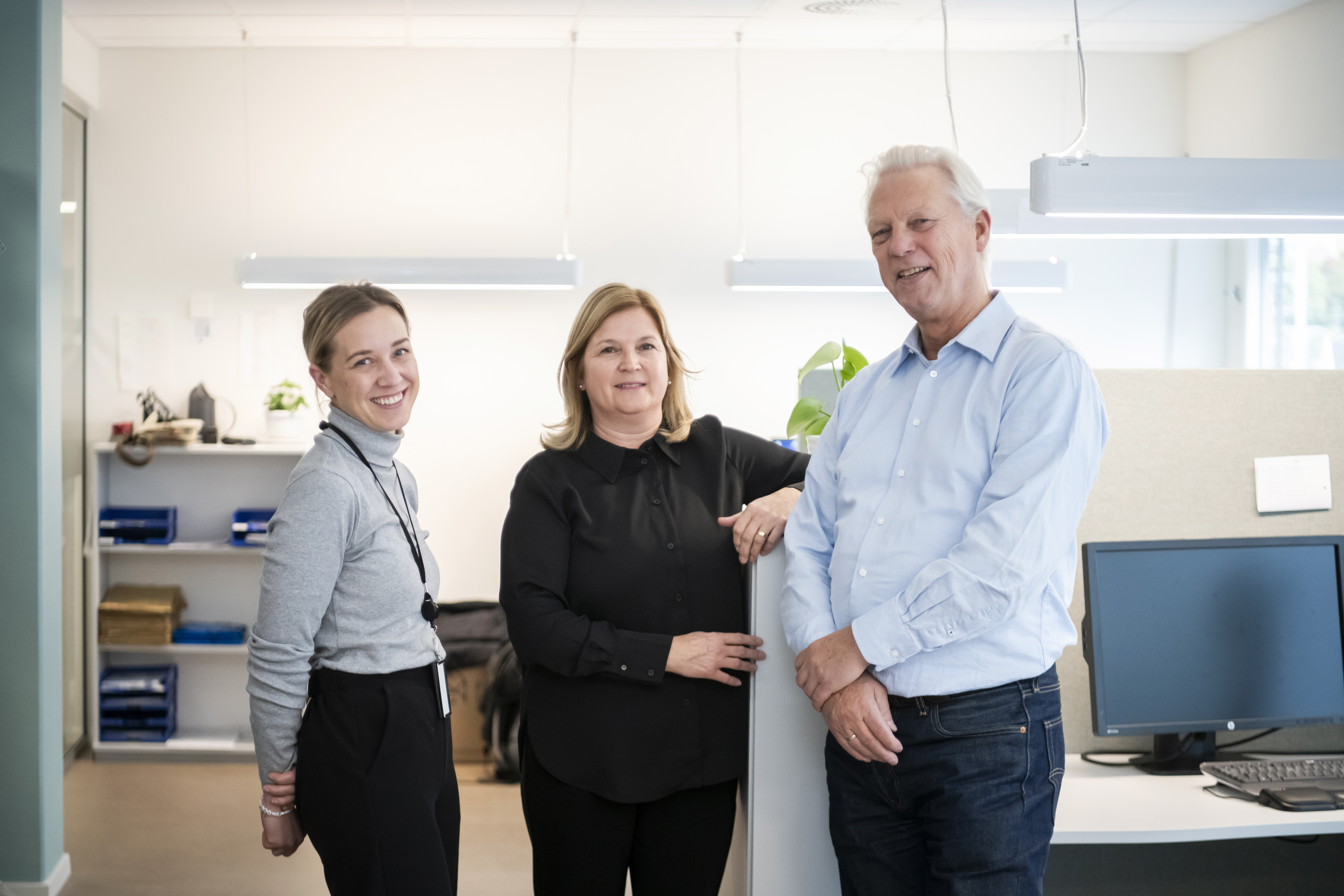 Tre kontoransatte smiler mot kamera