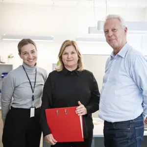 Tre smilende kontoransatte med en rød perm