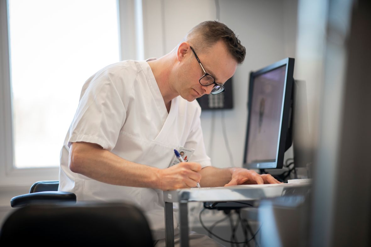 Mannlig ansatt sitter foran pc skjermer og leser i papirer