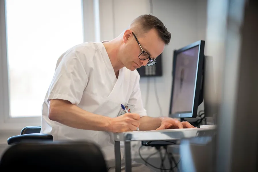 Mannlig ansatt sitter foran pc skjermer og leser i papirer