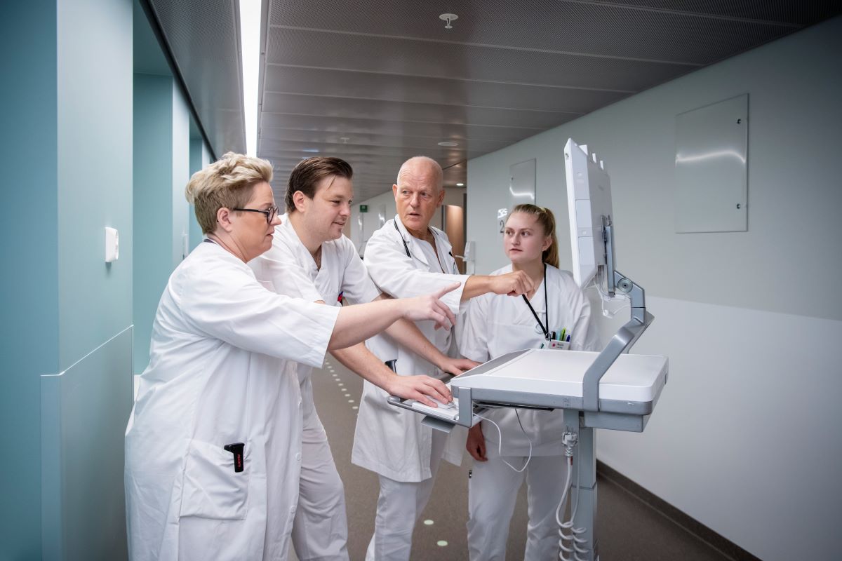 Fire helseansatte diskuterer foran en dataskjerm