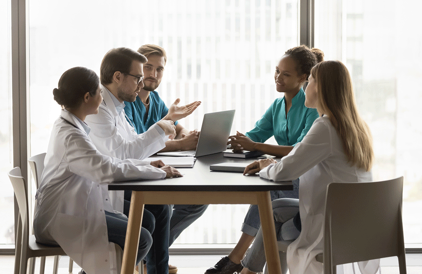 En gruppe helsearbeidere sitter rundt et bord , snakker sammen, en bærbar datamaskin på bordet