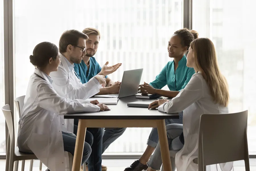 En gruppe helsearbeidere sitter rundt et bord , snakker sammen, en bærbar datamaskin på bordet