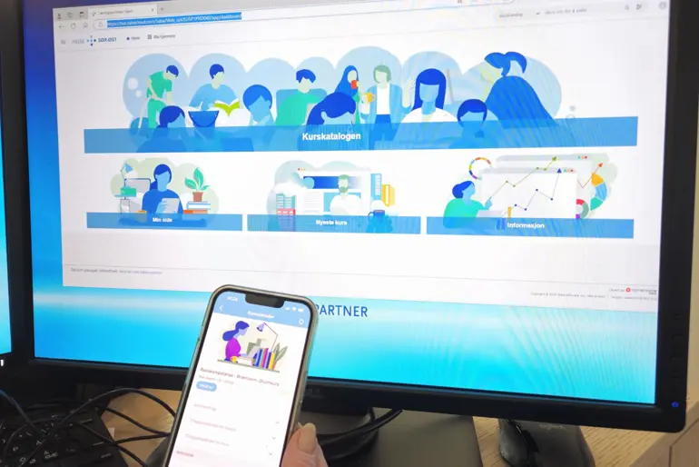 En hånd som holder en telefon foran en dataskjerm