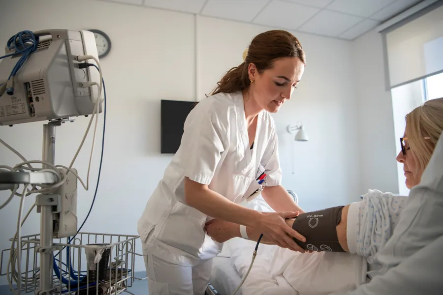 En kvinne som setter på en måler på armen til en kvinnelig pasient i sengen.