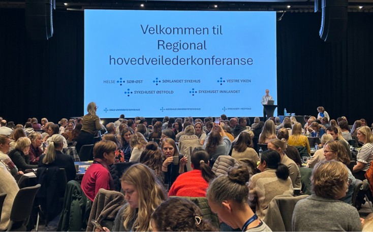 En gruppe mennesker som sitter i et rom med en stor skjerm