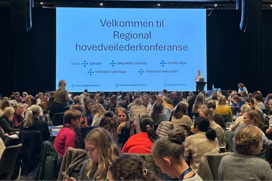 En gruppe mennesker som sitter i et rom med en stor skjerm